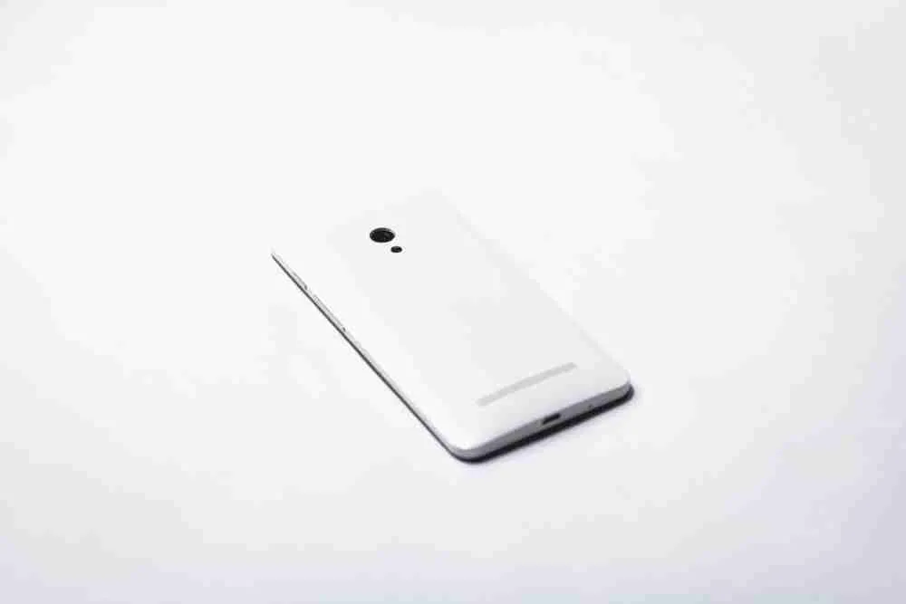 A white smartphone with a camera lies isolated on a guaranteed mobile phone contract background, exemplifying minimalistic design and modern technology.