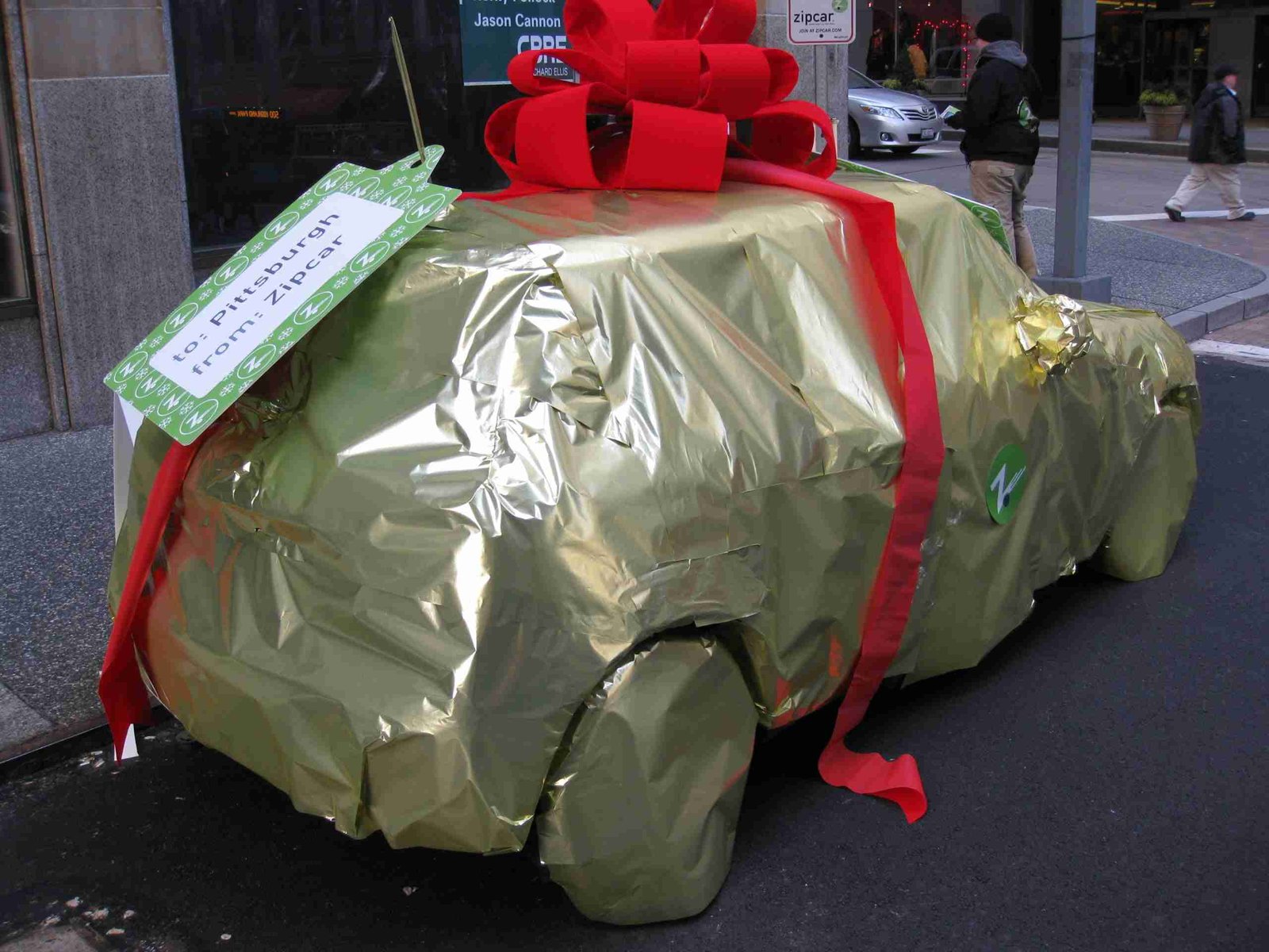 A car wrapped in golden paper and tied with a large red ribbon, resembling a gift, parked on a city street. Phones With Free Gifts Bad Credit. guaranteed phone contracts with free gift