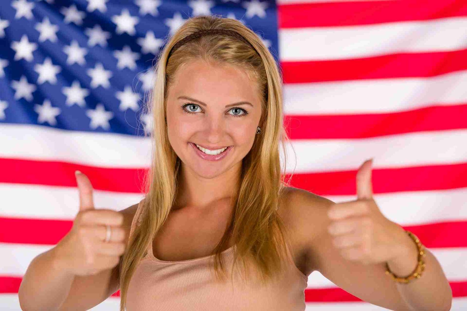 A cheerful woman giving two thumbs up in front of an american flag.