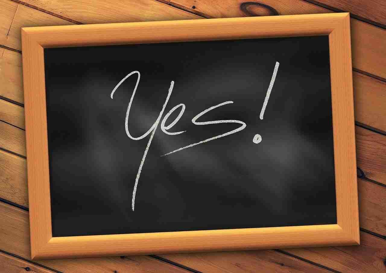 A wooden-framed chalkboard with the word "yes!" written on it in cursive, conveying a positive affirmation or agreement, displayed against a wooden plank background. yes phone contracts