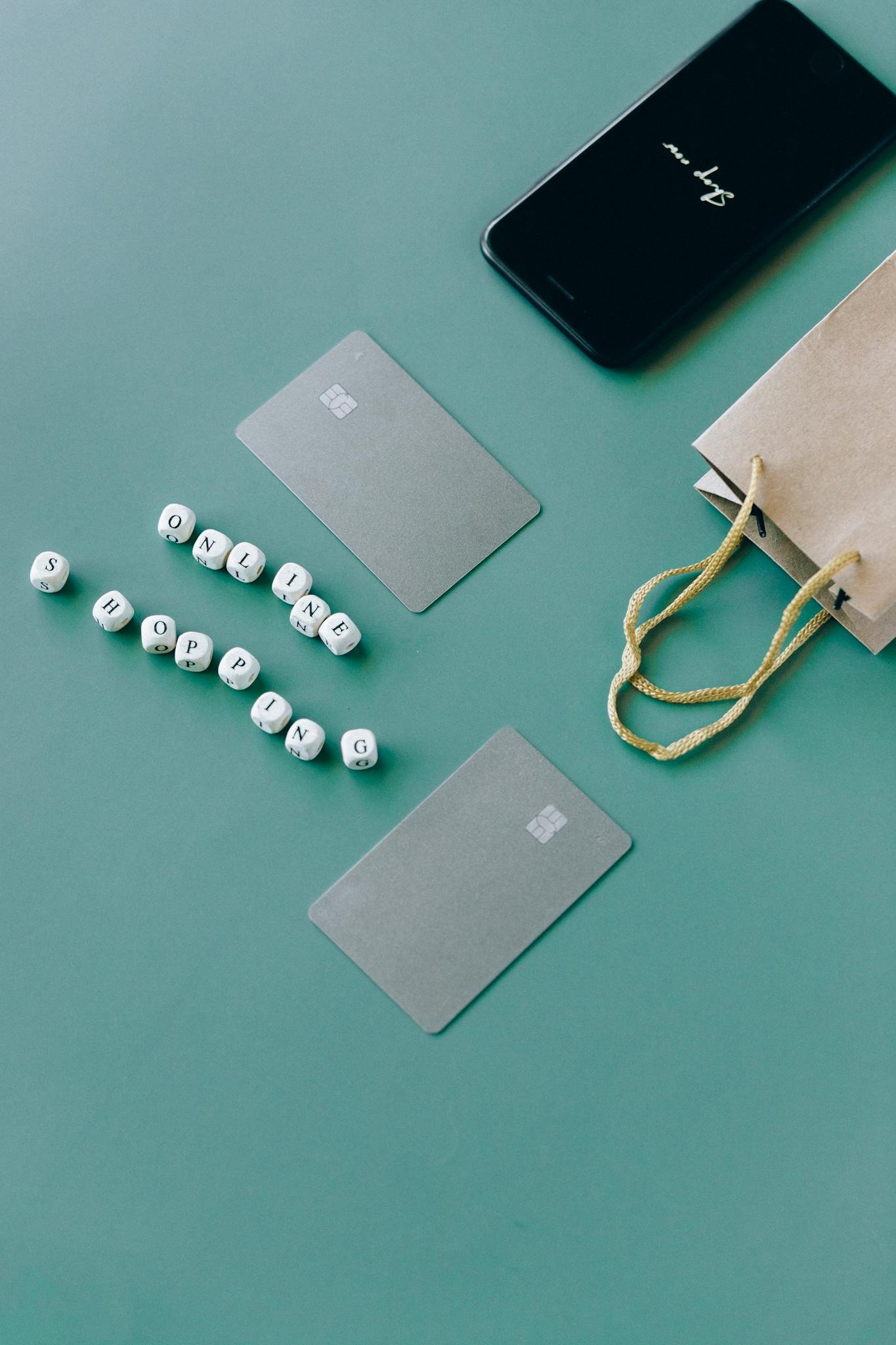 Home 2 Top view of bank cards, smartphone, and shopping bag on green surface, illustrating online shopping.