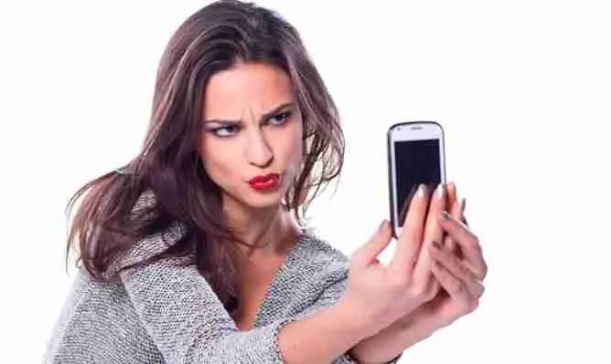 A perplexed woman skeptically looking at her mobile phone with a slight frown, possibly confused or annoyed by something she has encountered on her device, such as the terms of guaranteed mobile phone contracts.
